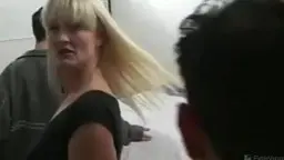 Blonde MILF in engem schwarzen Kleid steht neben einem Mann vor grüner Hausfassade