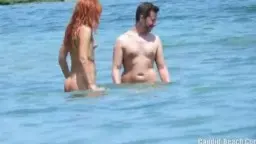 Nackte rothaarige Frau und muskulöser Mann stehen eng umschlungen im flachen Meerwasser