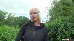 Lachende blonde MILF mit weißem Haar im schwarzen Hoodie vor üppigem Grün im Park