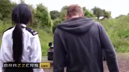 Schwarze Polizistin mit Pferdeschwanz steht mit einem Mann in dunkler Kapuzenjacke auf einer Waldlichtung