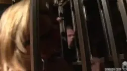 Blonde Frau von hinten in Metallkäfig gefesselt, Po rot gestriemt, Master mit Peitsche daneben