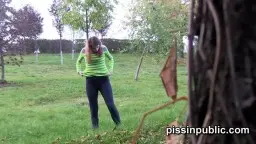 Frau in grünem Top und Leggings spreizt die Beine weit und pinkelt auf eine grüne Wiese