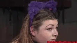 Frau im pink-schwarzen Zebraanzug kniet gefesselt über Holzbock** (8 Wörter)