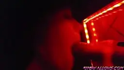 Frau kniet in rotem Licht und saugt Schwanz durch Gloryhole Loch