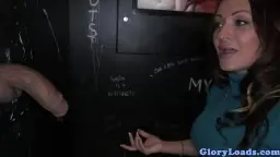 Attraktive MILF mit großen Augen kniet vor Glory Hole und greift nach dem großen Schwanz