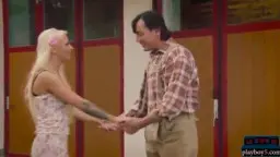 Blonde Frau im Dirndl greift einem Mann im Trägerhemd und grüner Hose in den Schritt vor einer Berghütte