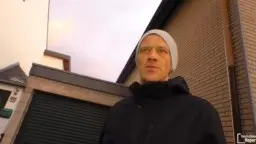 Reife blonde Frau mit Pelzkragen lächelt einen Mann mit weißer Mütze auf der Straße an
