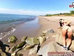 Schlanke MILF mit schwarzem Haar und pinkem Top posiert lasziv auf Felsen am Strand