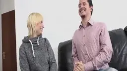 Blonde im Hoodie greift lächelnd zwischen die Beine des Nachbarn auf schwarzer Ledercouch