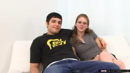 Lächelndes Nerdgirl mit Brille und Pferdeschwanz sitzt eng neben ihrem Freund auf weißer Couch