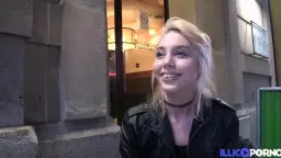 Freche blonde Frau mit Choker lächelt frech vor beleuchtetem Hauseingang
