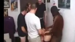 Junge Frau in weißem Pullover wird von einem Mann in dunkler Hose von hinten gepackt, chaotisches Zimmer im Hintergrund
