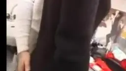 Junges Mädchen in weißem Pullover wird von einem Mann in dunkler Hose von hinten gepackt, chaotisches Zimmer im Hintergrund
