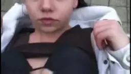 Nahaufnahme einer jungen Frau mit geöffneter weißer Jacke und heruntergezogenem schwarzen Top, die direkt in die Kamera schaut