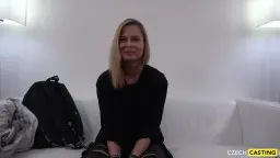 Blonde junge Frau sitzt auf weißem Sofa mit Rucksack