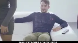 Zwei Latinaschwestern in engen Kleidern sitzen nah bei einem Mann auf weißem Sofa im hellen Wohnzimmer