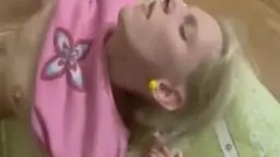 Blonde in pinkem Shirt liegt auf dem Bauch und saugt genussvoll an einem Schwanz