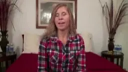 Reifes Paar sitzt angespannt nebeneinander auf rotem Sofa, er im schwarzen T-Shirt, sie im grauen Top, Wohnzimmer-Setting.
